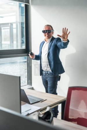 Téléchargez les photos : Photo verticale d'un homme d'affaires occasionnel faisant un geste en utilisant de nouvelles lunettes de réalité mixte dans le bureau - en image libre de droit