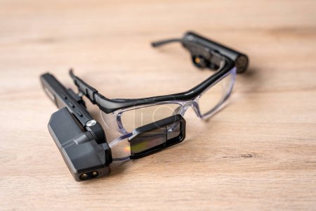 Vista superior en la mesa de madera de un pequeño dispositivo portátil de gafas de realidad mixta conectado a las gafas