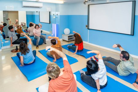 Erhöhte Rückansicht einer Gruppe von männlichen und weiblichen Behinderten, die sich während eines gemeinsamen Yoga-Kurses dehnen