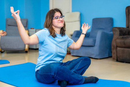 Frau mit besonderen Bedürfnissen genießt während des Yoga-Kurses sitzend in Lotusposition und mit erhobenen Armen