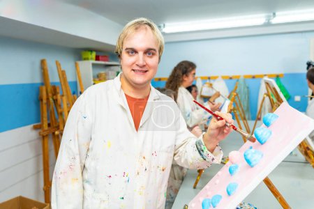 Retrato de un hombre con discapacidad mental con bata de laboratorio blanca sonriendo a la cámara en la clase de pintura