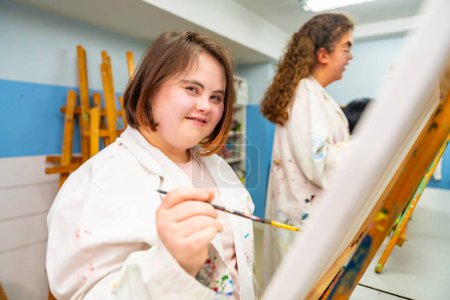 Portrait d'une femme atteinte du syndrome du duvet dans une classe de peinture souriant à la caméra