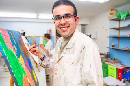 Hombre discapacitado mirando a la cámara y sonriendo feliz mientras pinta sobre lienzo