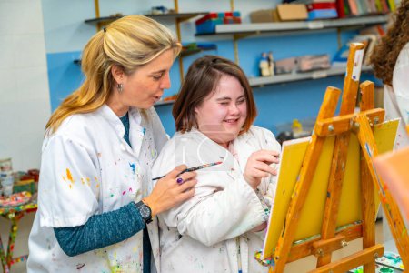 Maestra caucásica adulta ayudando a una mujer sonriente con síndrome de Down durante la clase de pintura