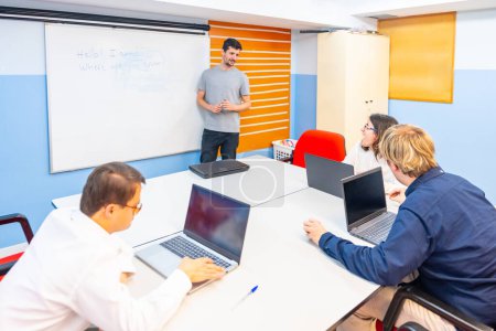 Menschen mit besonderen Bedürfnissen besuchen einen IT-Kurs mit Laptop, während Lehrer die Verwendung von Whiteboards erklären