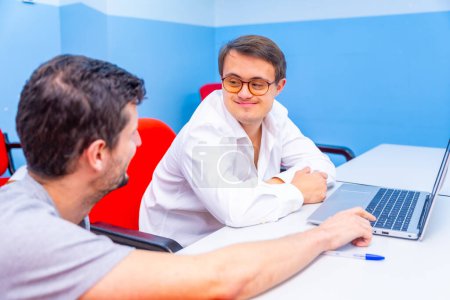 Happy and relaxed man with down syndrome and teacher talking during IT computing class