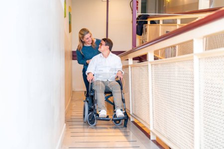 Téléchargez les photos : Infirmière aimable et homme handicapé avec le syndrome du duvet parlant tout en utilisant fauteuil roulant - en image libre de droit