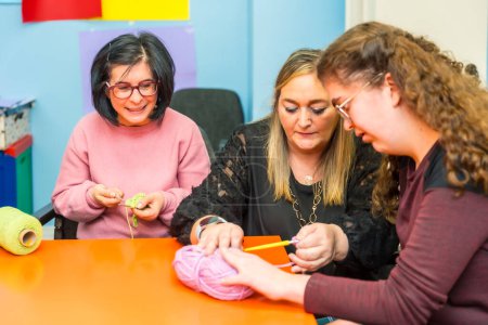 Photo for Women with intellectual disabilities and teacher learning how to knit clothes with wool - Royalty Free Image