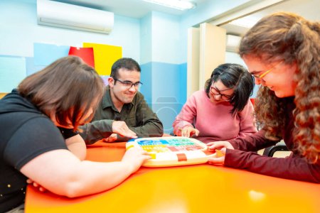 Groupe de personnes handicapées jouant ensemble à des jeux de société en s'amusant dans un centre de jour pour les personnes ayant des besoins spéciaux