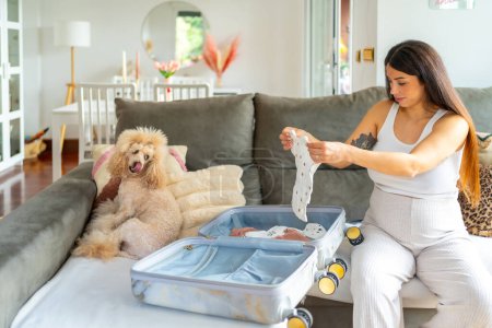 Téléchargez les photos : Femme enceinte préparant une valise pour aller à l'hôpital assis sur un canapé à côté d'un chien - en image libre de droit