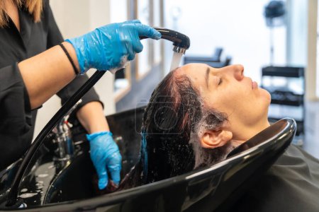 Téléchargez les photos : Coiffeur laver les cheveux d'une femme dans un évier dans un salon de beauté - en image libre de droit