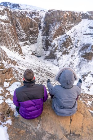 Una pareja meditando en invierno en Islandia en la cascada congelada de Hengifoss