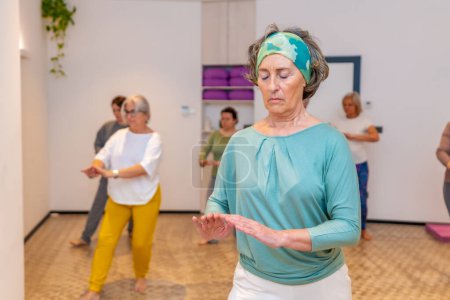 Concentrated woman closing eyes and breathing while exercising during qi gong class