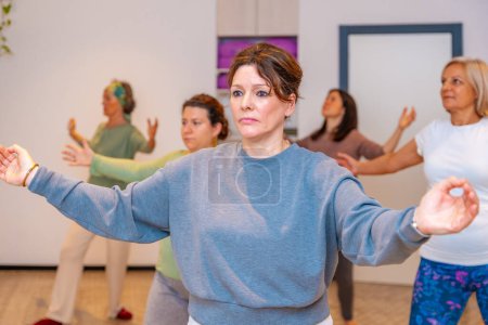 Group of mature adult and caucasian sportive women opening arms during qi gong class