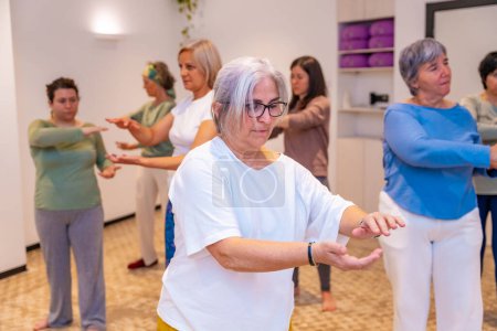 Mature adult caucasian concentrated women exercising in pairs during Qi gong class