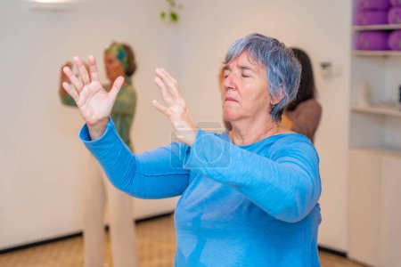 Close-up of an elder woman closing eyes and raising arms in cercle during qi gong class