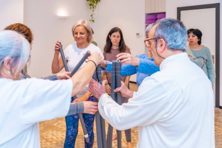 Male mature Qi gong instructor delivering a tube to exercise to the female members of the class