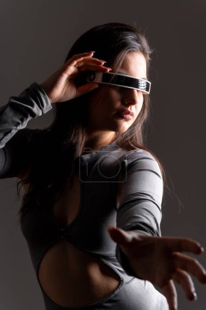 Retrato de estudio con fondo gris de una sensual mujer futurista usando gafas de realidad virtual