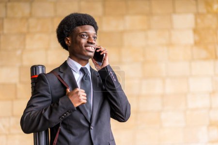 Horizontal photo with copy space of an young african american architect wearing suit talking to the mobile phone in the city next to a urban wall