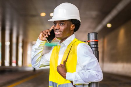 Photo for Side view close-up portrait of a busy young african architect wearing protective gear talking to the mobile in the city - Royalty Free Image