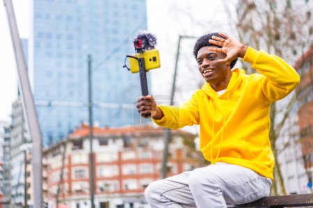 Photo for Side view photo with copy space of a young african content creator waving at camera recording a video in the city - Royalty Free Image