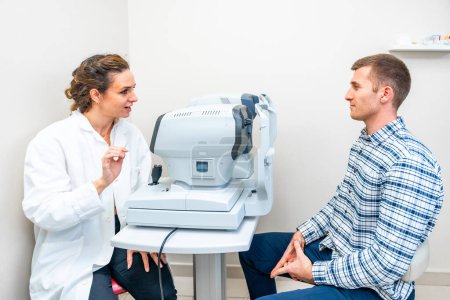 Téléchargez les photos : Ophtalmologiste féminine expliquant la procédure d'un scan à un patient dans une clinique - en image libre de droit
