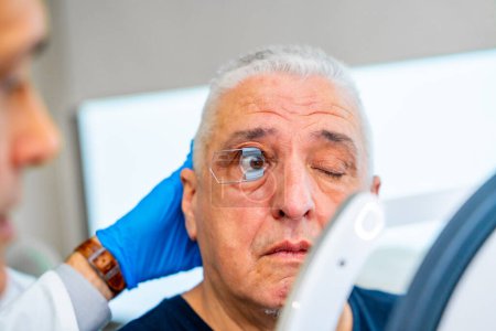 Augenarzt, der ein Werkzeug anwendet, um das Auge eines Mannes zu erhalten, das für den Scan geöffnet ist