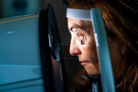 Nahaufnahme einer reifen Frau mit Augenöffner, die sich während einer Laserbehandlung gegen Glaukom lehnt