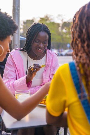 Vertikales Foto von drei jungen afrikanischen Freundinnen, die Nachos in einem Bürgersteig-Restaurant essen