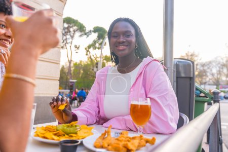Lächelnde afrikanische junge Frau isst mit Freunden Nachos in einem Restaurant unter freiem Himmel
