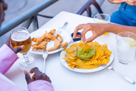 Hände einer Frau, die eine Nacho in Guacamole-Soße taucht und mit Freunden in einem Restaurant speist