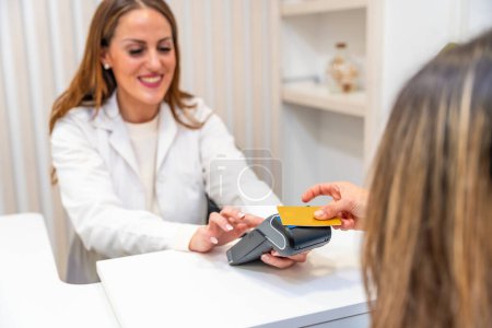 Téléchargez les photos : Vue arrière d'une cliente payant par carte de crédit à la réception d'une clinique d'esthéticienne - en image libre de droit