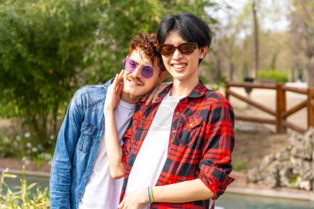 Photo for Portrait of a multi-ethnic gay couple smiling at camera standing together in a park - Royalty Free Image
