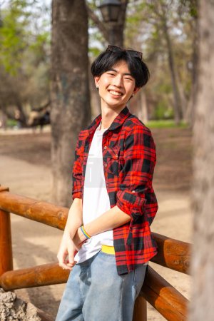 Photo for Vertical portrait of an asian gay man standing in a park smiling at camera - Royalty Free Image