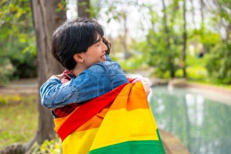 Multiracial gay couple embrassant à l'intérieur un lgbt drapeau debout dans un parc