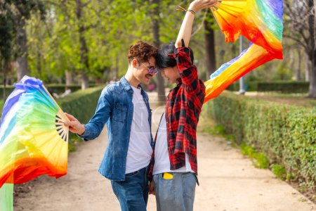 Seitenansicht eines multiethnischen schwulen Paares, das mit Regenbogenfächern tanzt