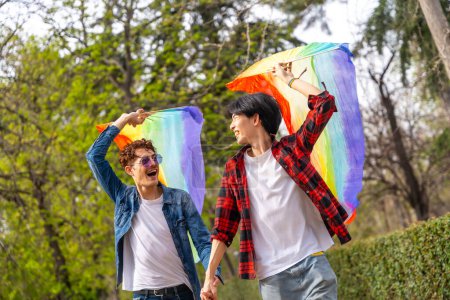 Photo for Happy multi-ethnic gay young men raising lgbt flags in a park - Royalty Free Image
