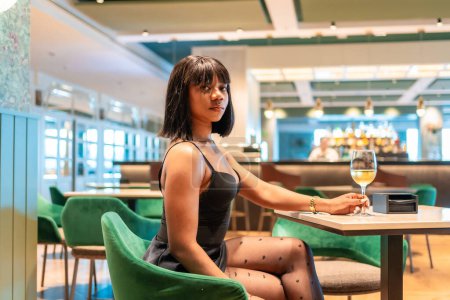Téléchargez les photos : Vue de côté portrait de trois quarts de longueur d'une femme africaine sensuelle buvant du vin dans un restaurant de luxe - en image libre de droit