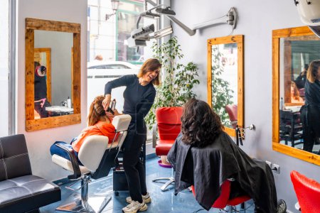 Téléchargez les photos : Coiffeur parlant et assistant clients féminins assis dans un salon de coiffure - en image libre de droit