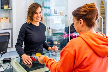 Téléchargez les photos : Vue arrière d'un client satisfait qui paie par carte de crédit dans un salon de coiffure - en image libre de droit