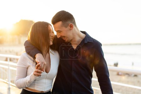 Tendre jeune couple caucasien embrassant flâner le long d'une promenade pendant le coucher du soleil