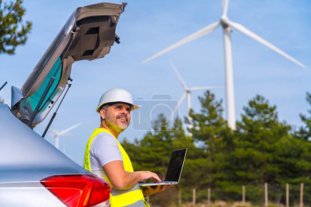 Male mature engineer controlling wind turbines using laptop in a wind energy park
