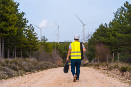 Rear view of a mature caucasian male worker walking along a path in a green energy park with wind turbines