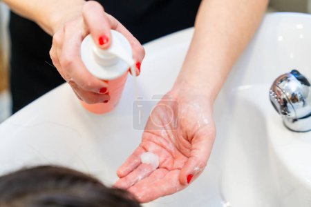 Close-up top view of an unrecognizable hairdresser pouring nourishing hair gel while washing the hair of a client