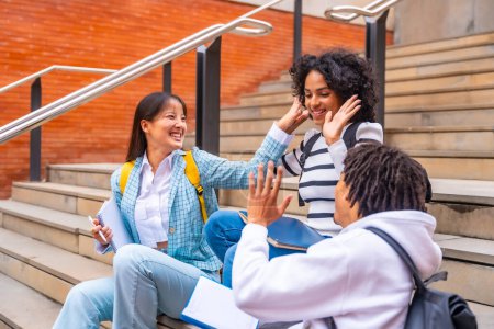 Téléchargez les photos : Heureux étudiants multi-ethniques assis sur le campus s'amuser détendu après les cours à l'université - en image libre de droit