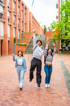 Foto vertical de tres estudiantes multiétnicos lanzando carpetas en el aire celebrando el final del curso