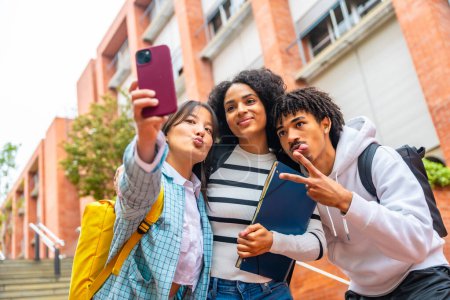 Retrato en ángulo bajo de tres estudiantes universitarios multirraciales felices tomando una selfie fuera del campus