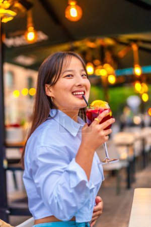 Vertical portrait of a chinese woman drinking tropical cocktail using straw in an outdoor terrace