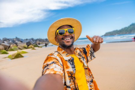 African smiling man taking selfie gesturing with thumb up in a sandy beach