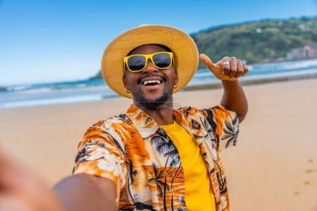 African young man taking selfie while gesturing with thumb up on the beach